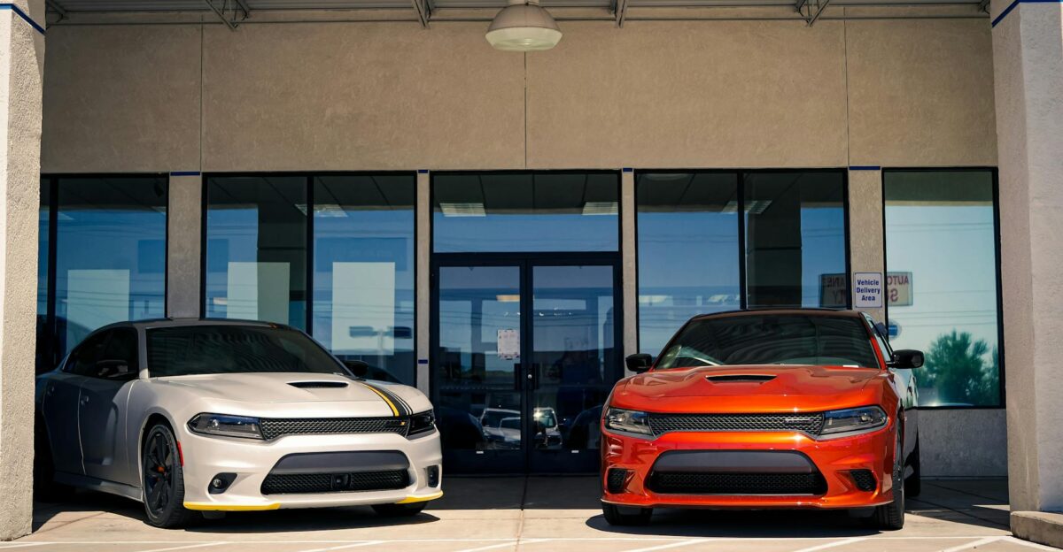 Two Dodge muscle cars parked outside a modern urban dealership entrance