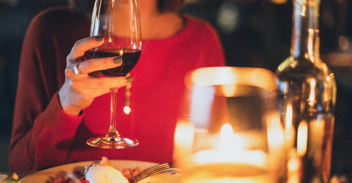 A woman enjoying red wine at a romantic candlelit dinner perfect for celebrations