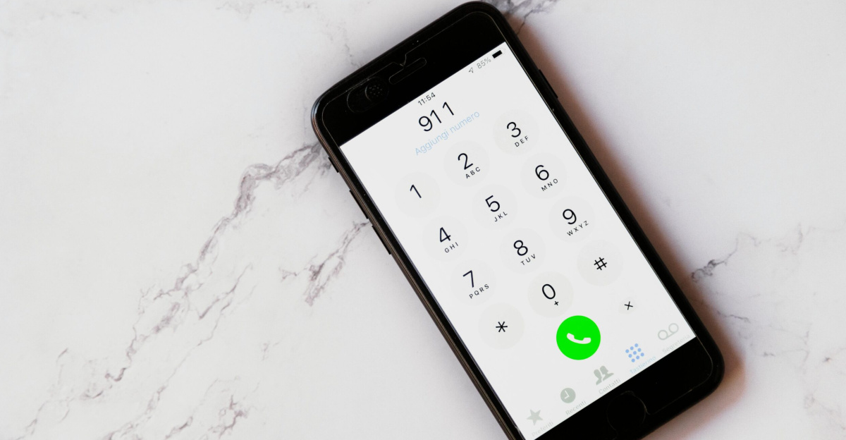 Close-up of a smartphone displaying the emergency number 911 on a white marble surface.