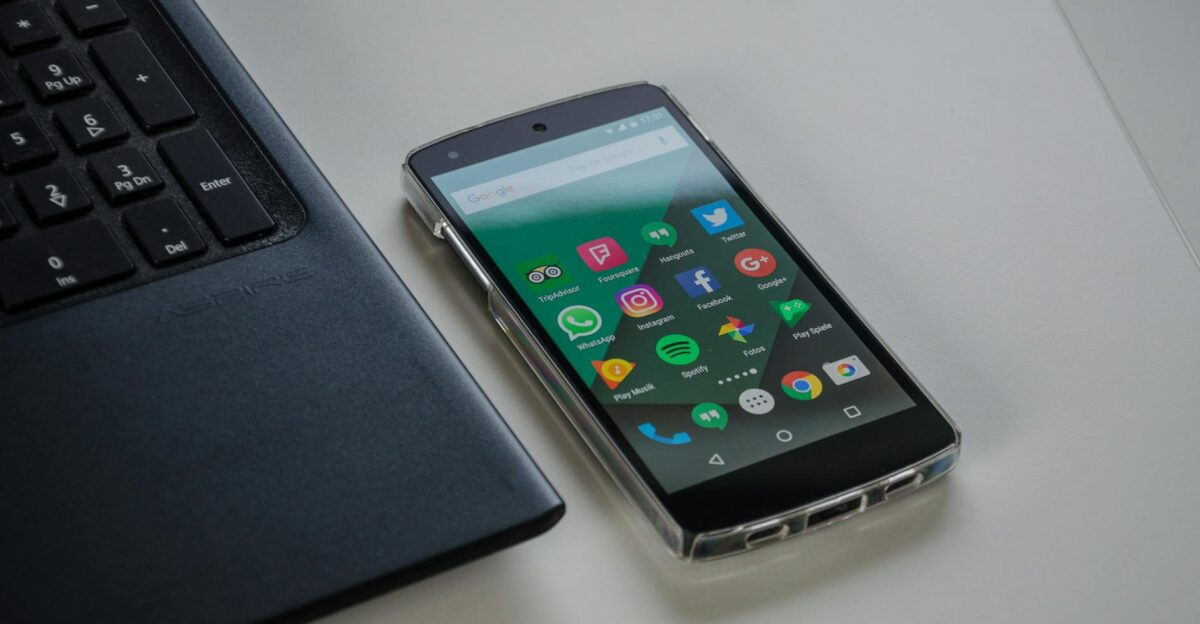 Smartphone on a table showing various social media apps beside a laptop keyboard