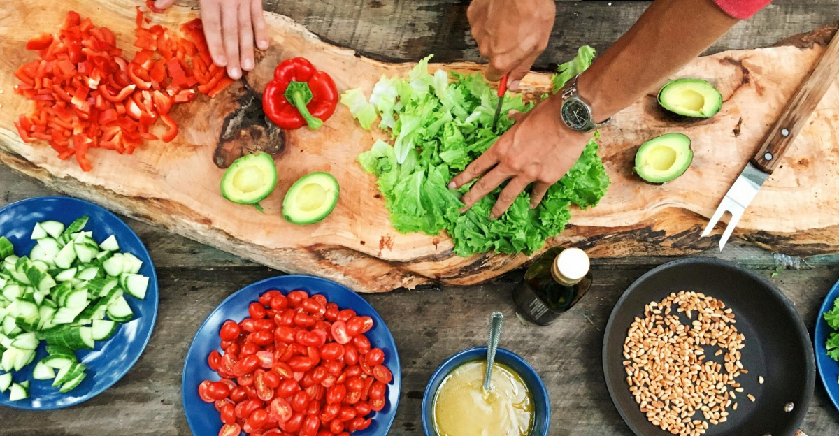 Fresh ingredients being prepared on a rustic wooden table, showcasing vibrant vegetables and hands at work.