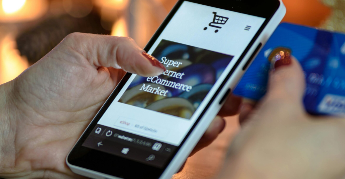Woman using smartphone for online shopping with credit card in hand, festive background lighting.