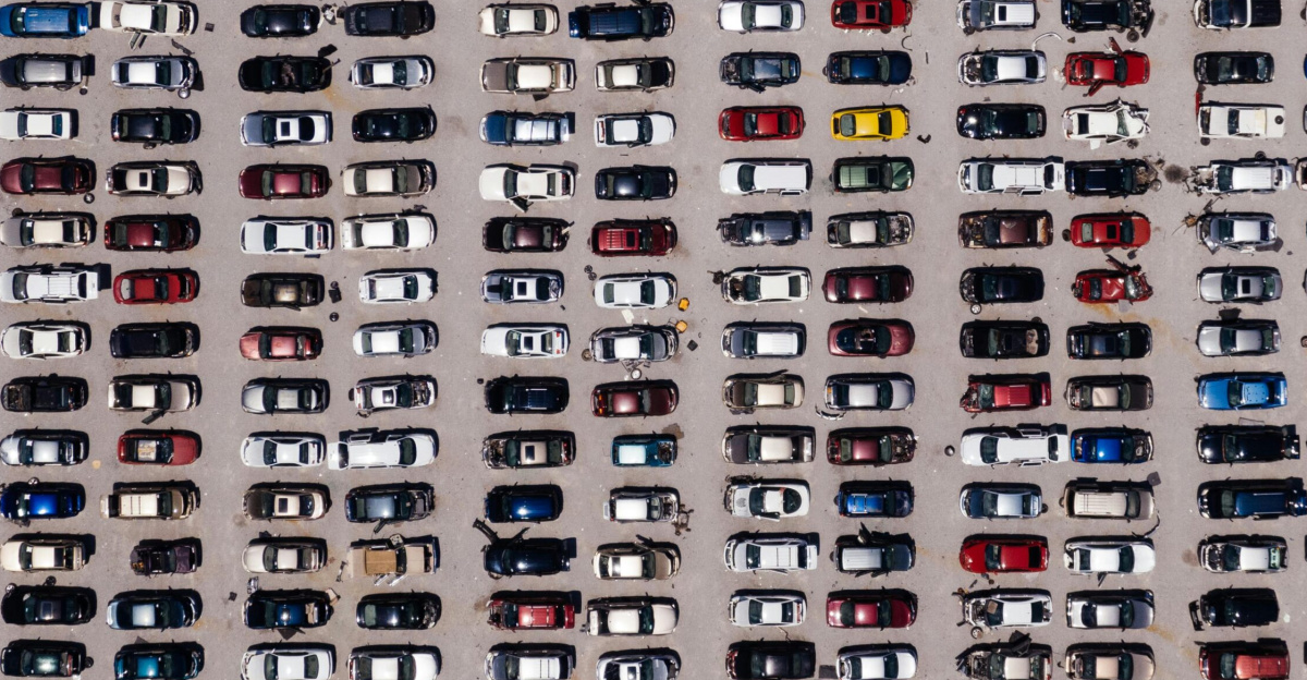 Top-down aerial shot of a large parking lot filled with rows of cars, showcasing organized symmetry.