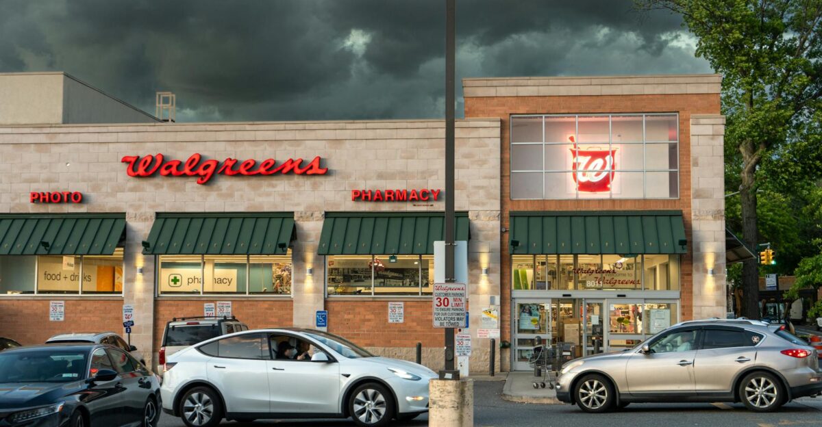 Exterior view of a Walgreens pharmacy under dark storm clouds with cars in the parking lot