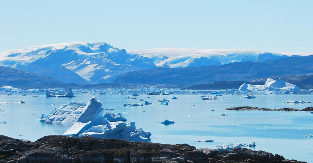 A breathtaking view of icebergs floating in a tranquil sea with distant snow-capped mountains, captured in Greenland.