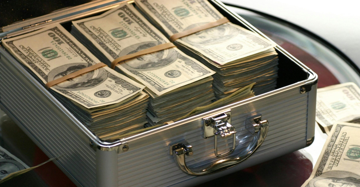 Open briefcase filled with stacks of hundred dollar bills on a glass table, representing wealth.