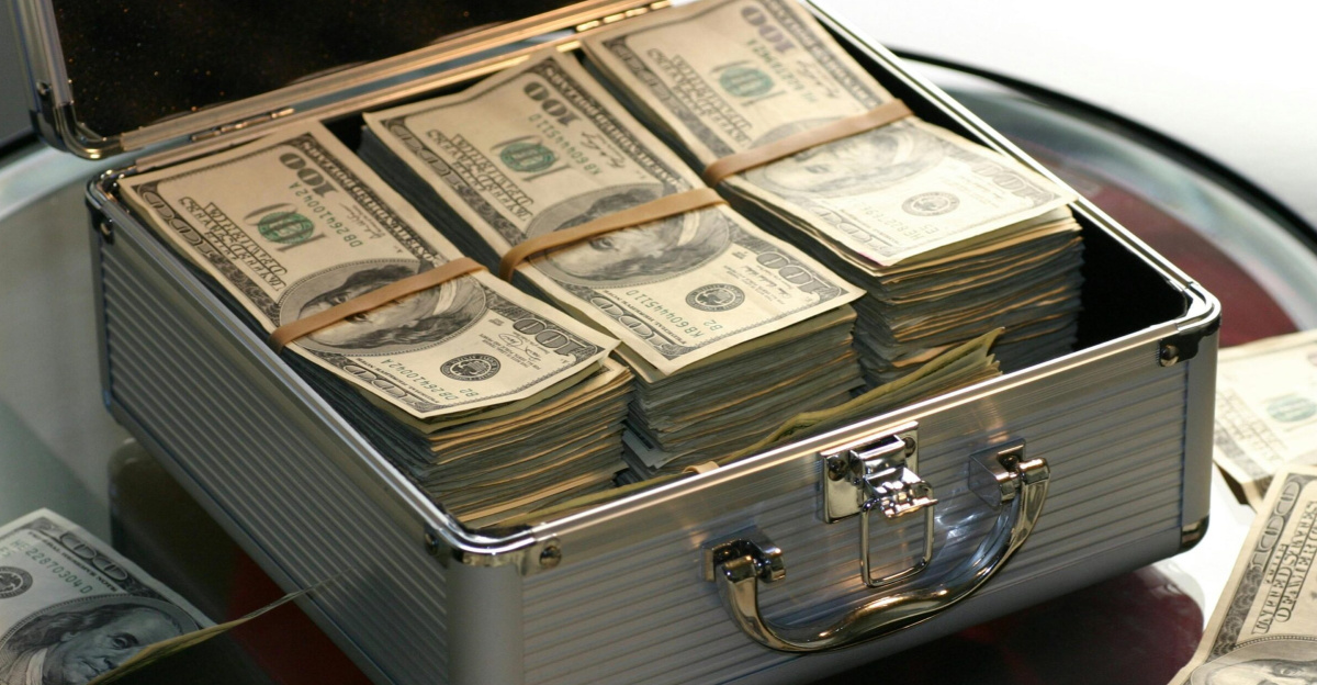 Open briefcase filled with stacks of hundred dollar bills on a glass table, representing wealth.