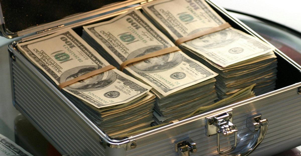 Open briefcase filled with stacks of hundred dollar bills on a glass table, representing wealth.