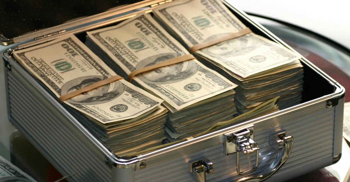 Open briefcase filled with stacks of hundred dollar bills on a glass table, representing wealth.
