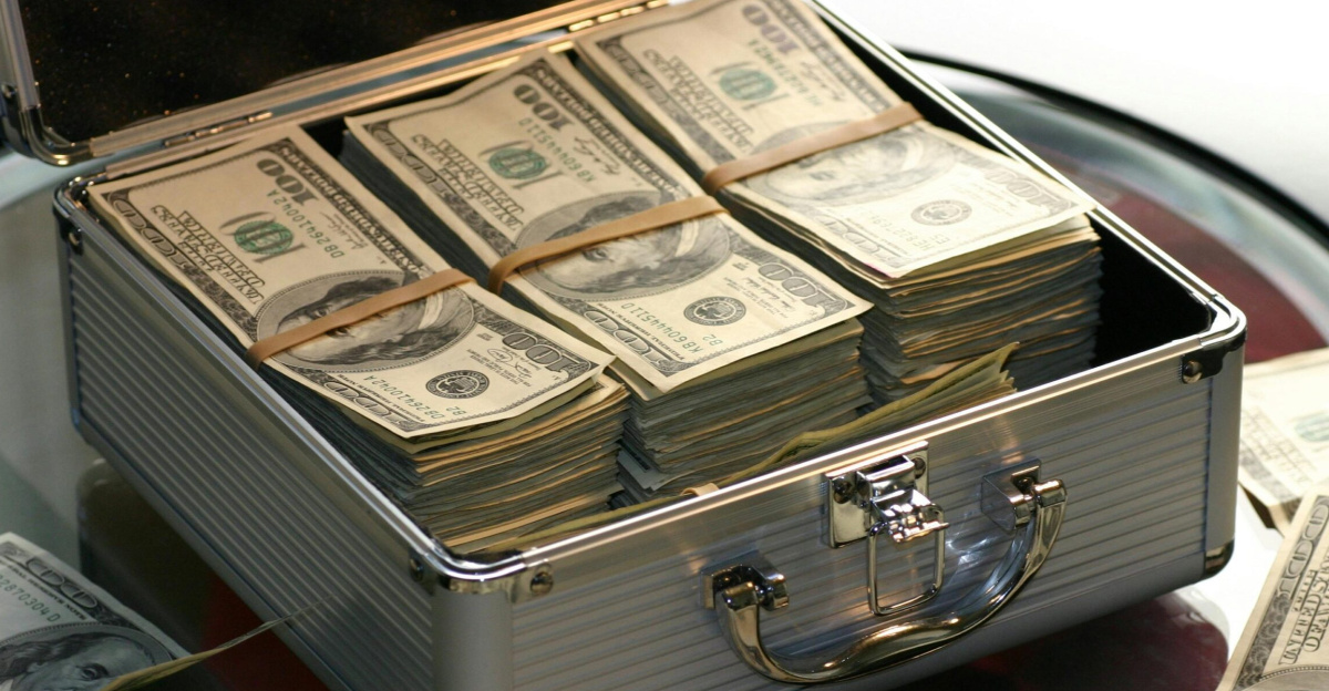 Open briefcase filled with stacks of hundred dollar bills on a glass table, representing wealth.