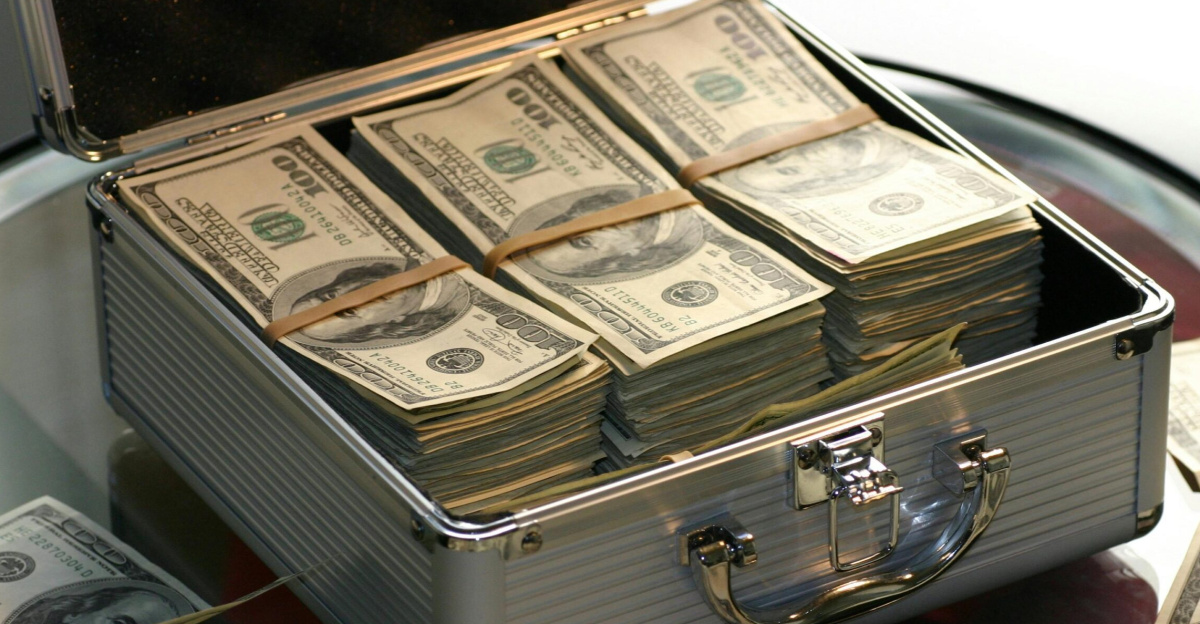 Open briefcase filled with stacks of hundred dollar bills on a glass table, representing wealth.