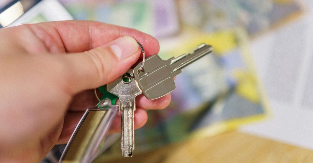 Close-up of keys in hand representing property ownership with blurred financial documents in the background