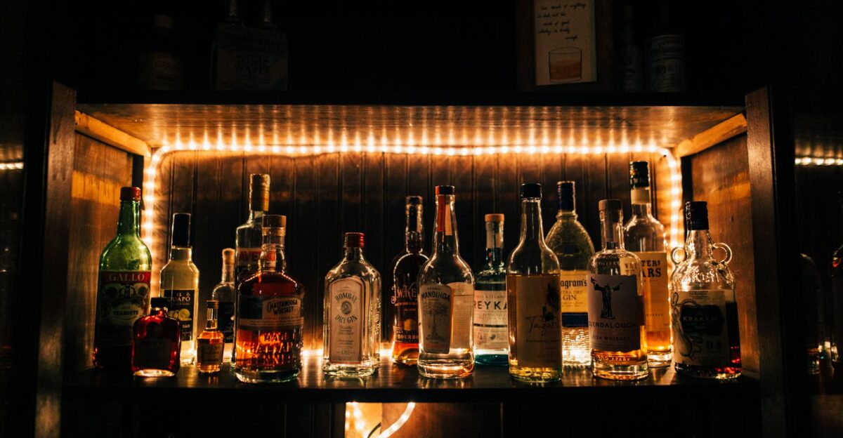 A stylish arrangement of various liquor bottles beautifully illuminated on a shelf in a dimly lit bar setting