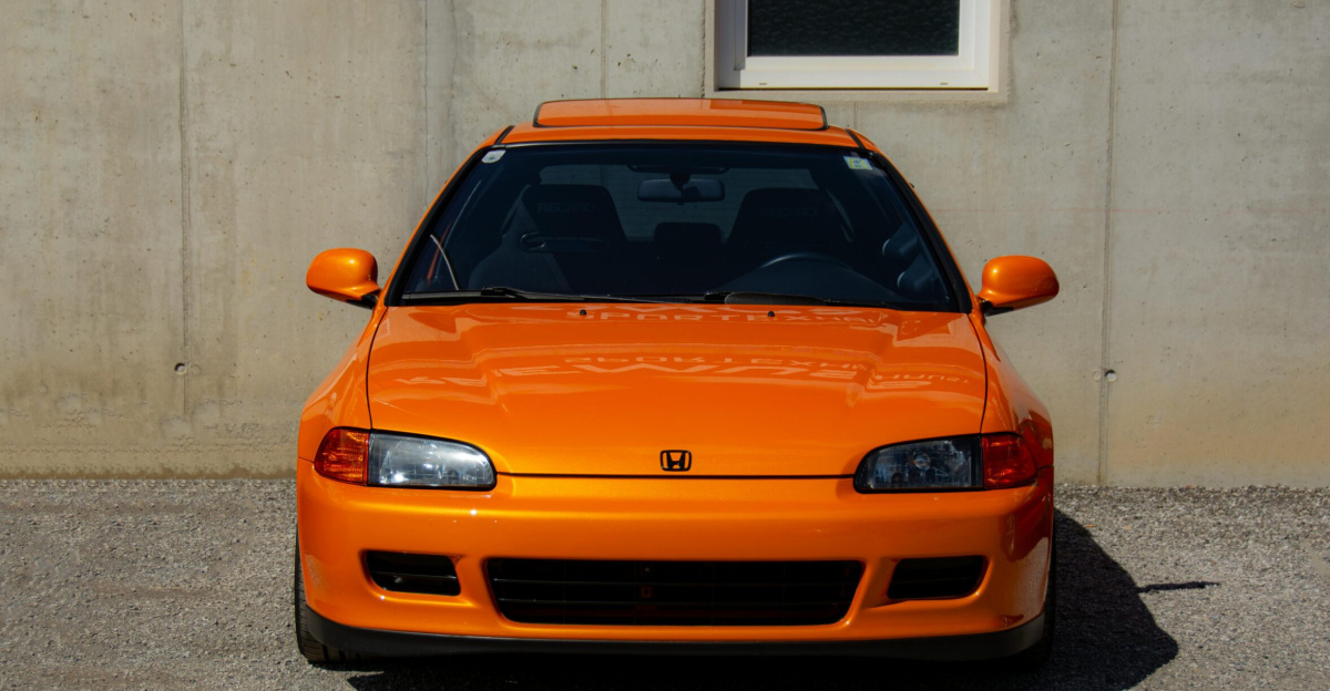 A vibrant orange Honda Civic parked outdoors at a car meet in Austria.