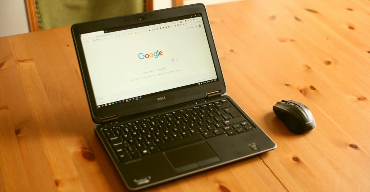 Black laptop and mouse on a wooden desk with Google homepage open