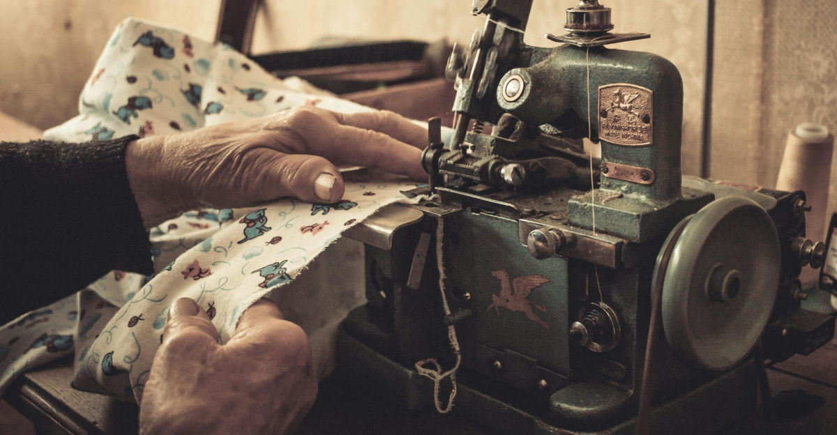Close-up of hands sewing with a vintage machine in a dimly lit room.