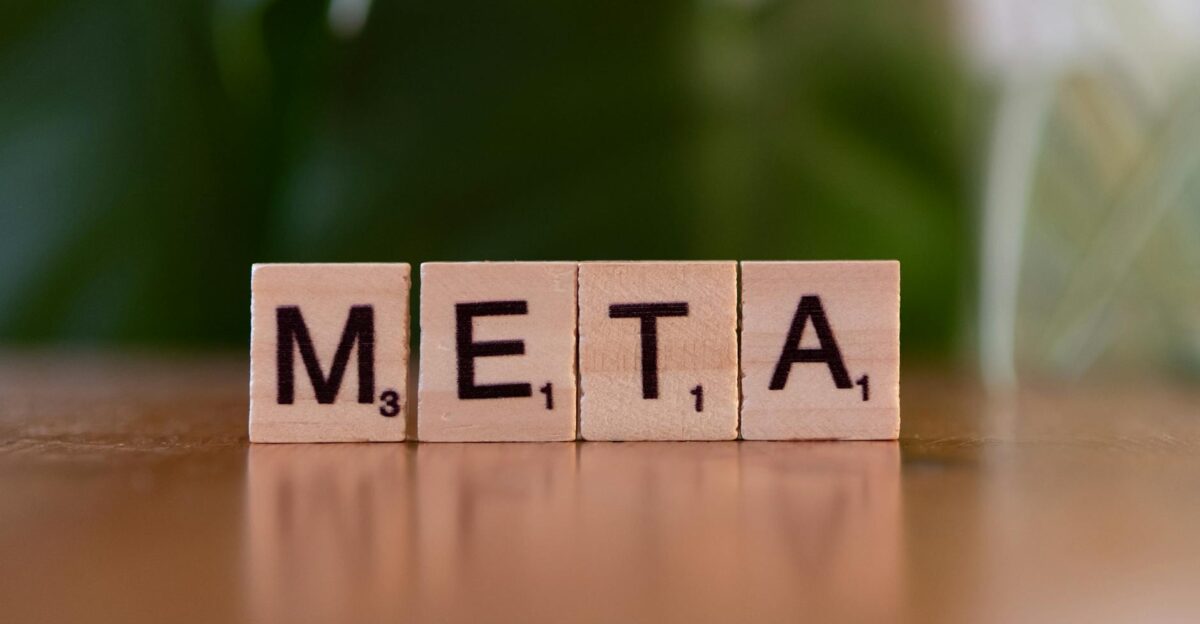 Wooden letter blocks spell META on a table with a blurred green background
