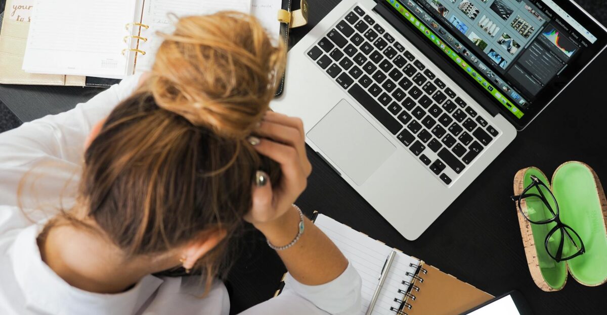 Overhead view of a stressed woman working at a desk with a laptop phone and notebooks