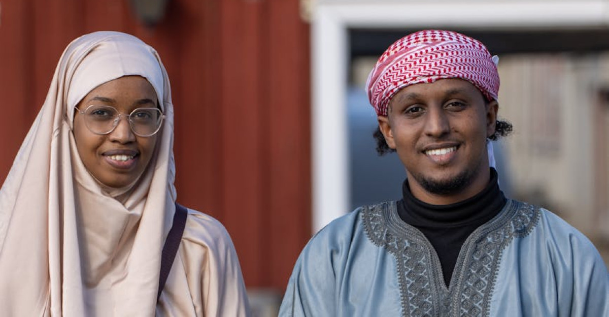 A portrait of two adults in traditional Somali clothing outdoors smiling and seated