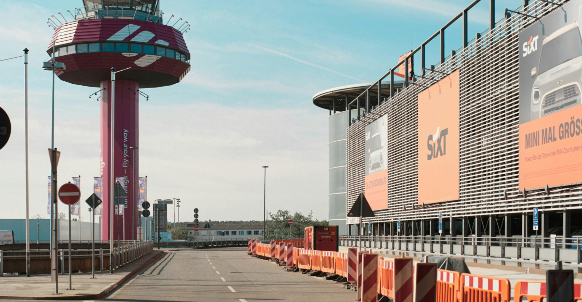 A vibrant air traffic control tower beside a Sixt advertisement display during a sunny day.