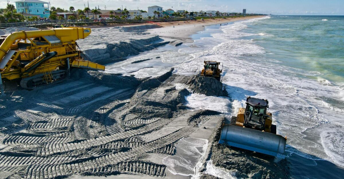 Heavy machinery working on beach coastline to manage erosion and restore sand