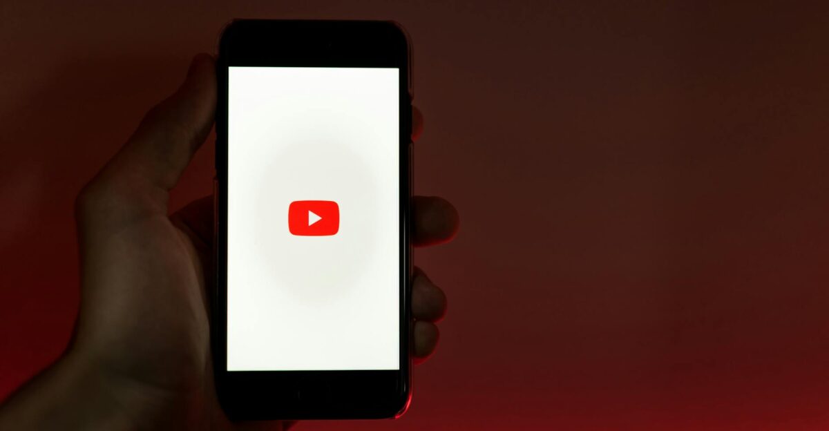 A hand holding a smartphone displaying the YouTube app against a red background