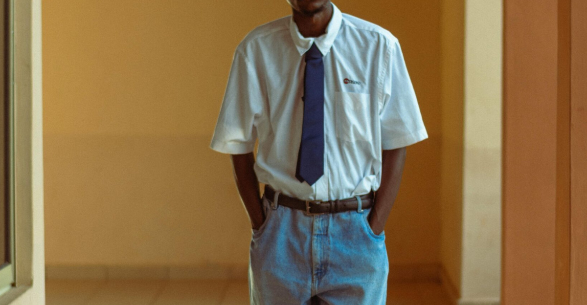 Young man in stylish casual attire poses in sunlit hallway, embodying urban fashion.
