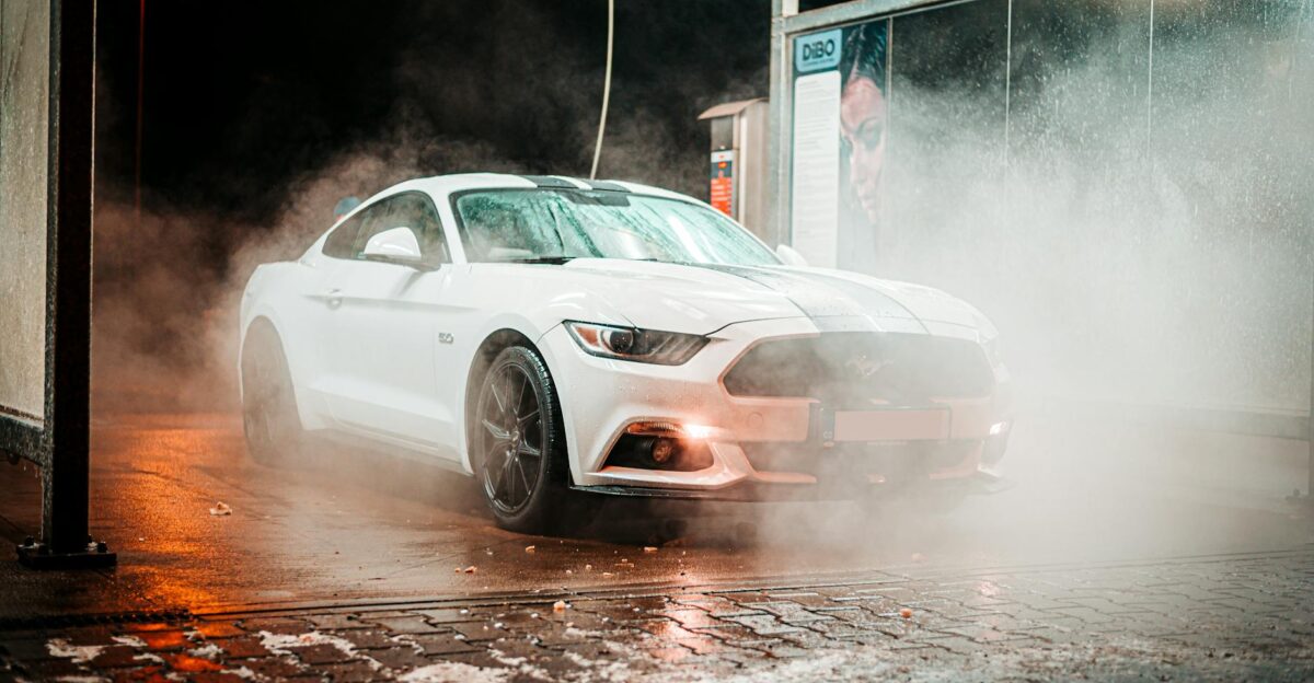 White Ford Mustang in a misty carwash setting illuminated at night in an urban environment