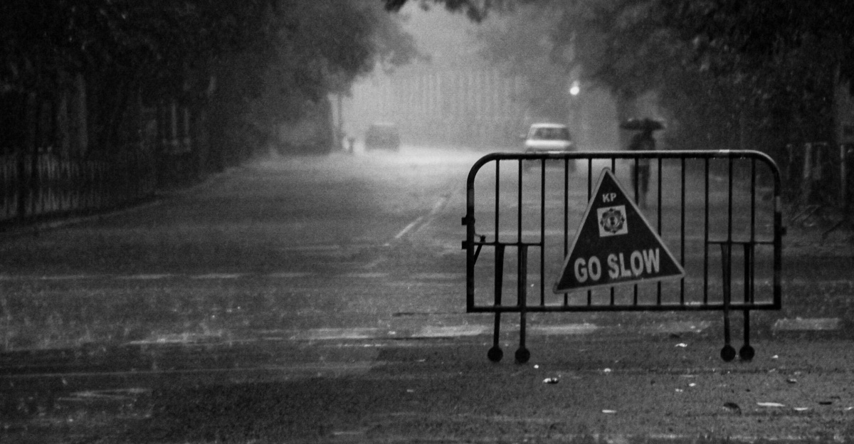 Black and white street scene in heavy rain with a cautionary 'Go Slow' sign.