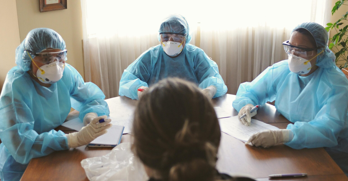 Group of healthcare workers in PPE having a discussion around a table indoors.