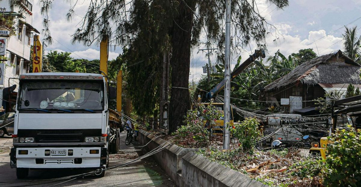 Street view of a truck near fallen power lines with trees and buildings.