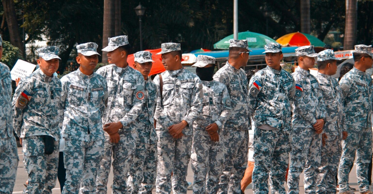 A group of soldiers in camouflage uniforms standing in line outdoors during the day.