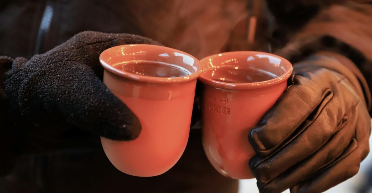Two hands clink warm mugs of gluhwein at a Kassel Christmas market