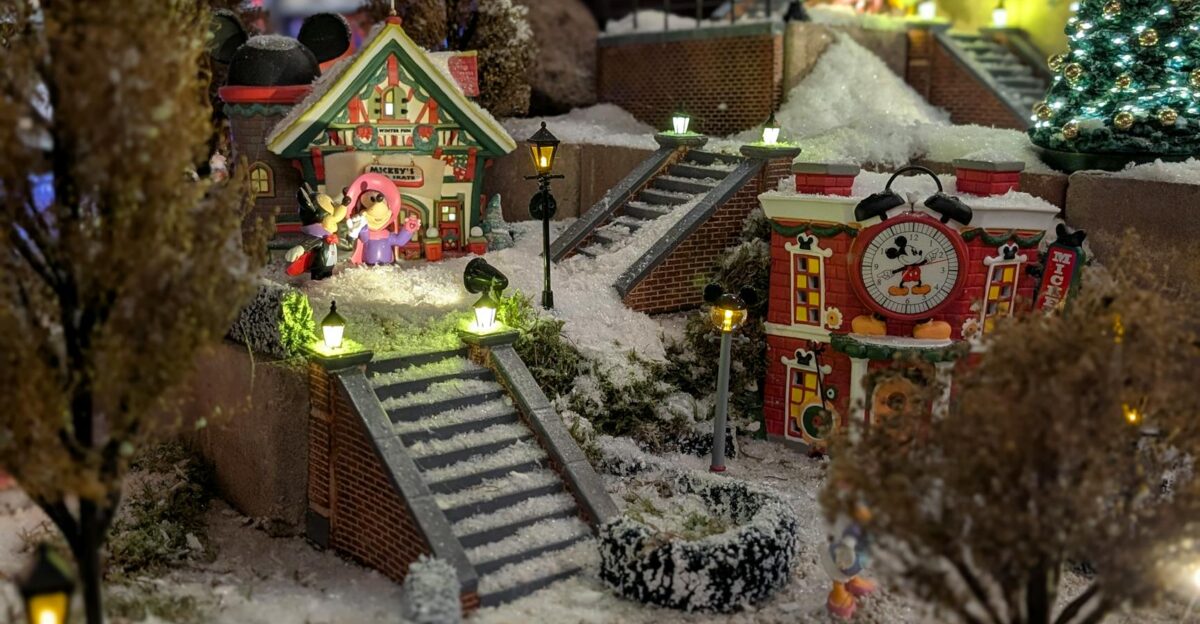 Festive miniature village scene featuring Mickey Mouse in a winter wonderland setting with lights and snow