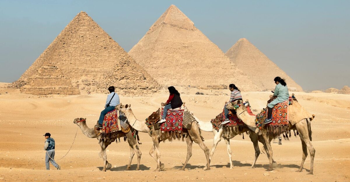 Tourists riding camels near the Great Pyramids of Giza Egypt under clear skies