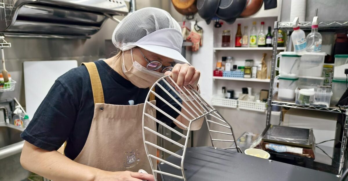 A chef in a kitchen apron and cap prepares equipment in a professional kitchen setting