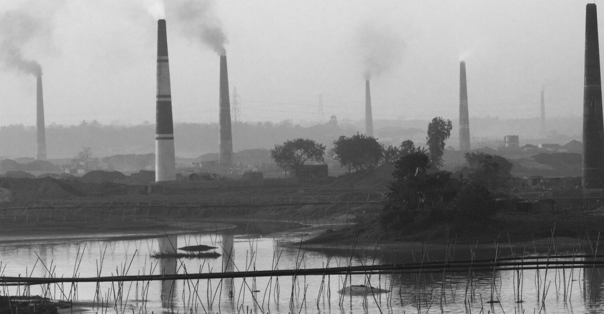 Black and white view of industrial smokestacks in Keraniganj, Bangladesh, reflecting in the river.