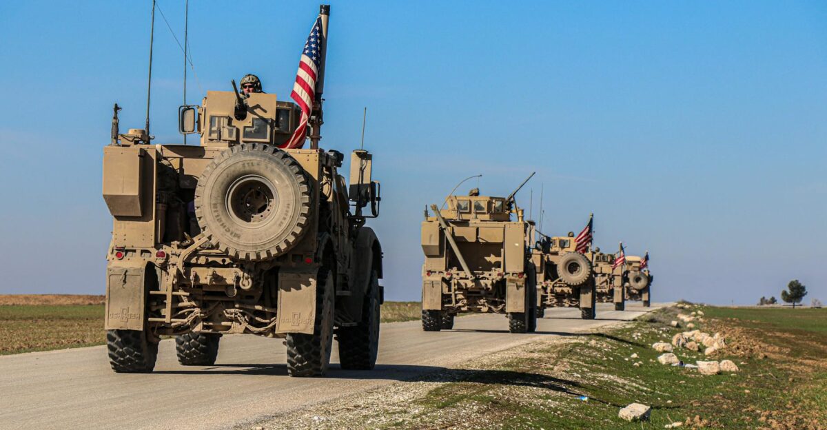 American military convoy driving through rural Syria under a blue sky