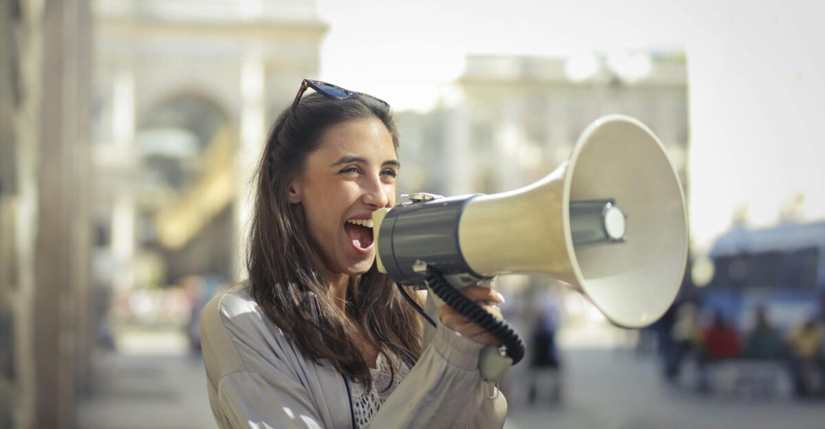 Cheerful young woman in a casual outfit shouting into a megaphone on a sunny day