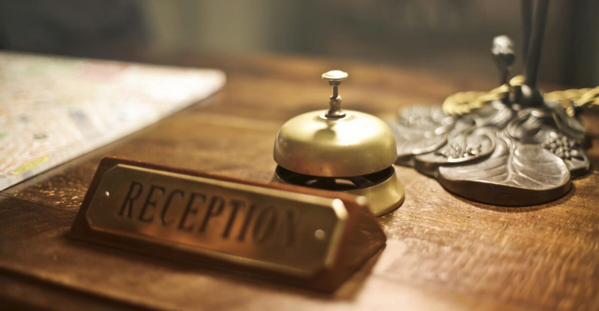 Old fashioned golden service bell and reception sign placed on wooden counter of hotel with retro interior