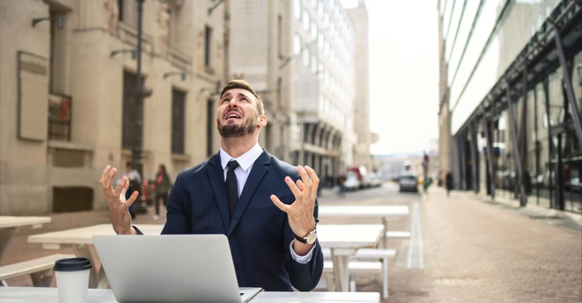 Businessman in suit showing frustration at outdoor table with laptop and coffee
