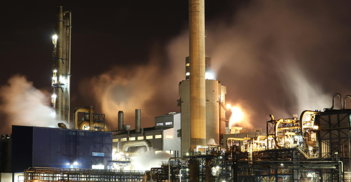 A nighttime view of an industrial factory with smokestacks emitting smoke, highlighting energy production and pollution.