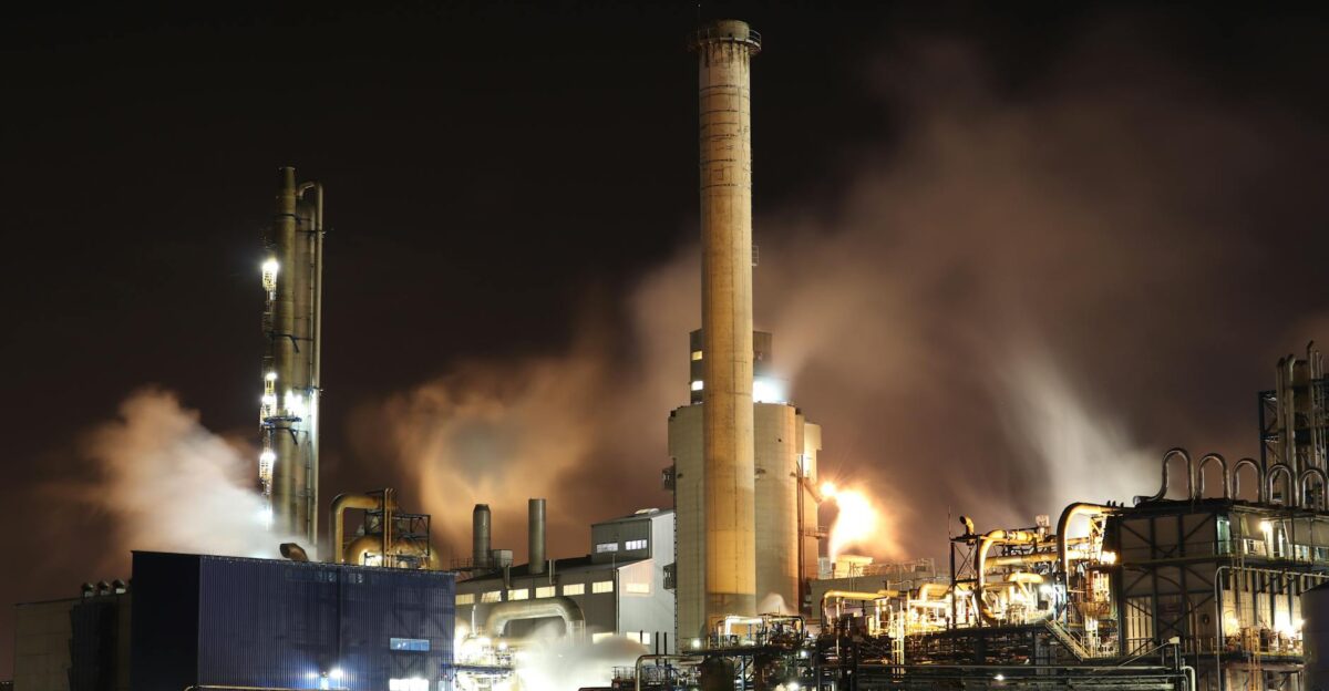 A nighttime view of an industrial factory with smokestacks emitting smoke highlighting energy production and pollution