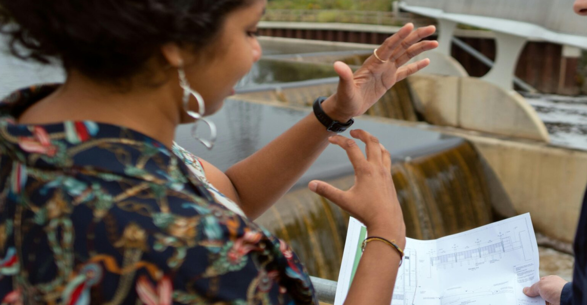 Two engineers discussing plans by a water project site. Collaborative teamwork on hydropower.