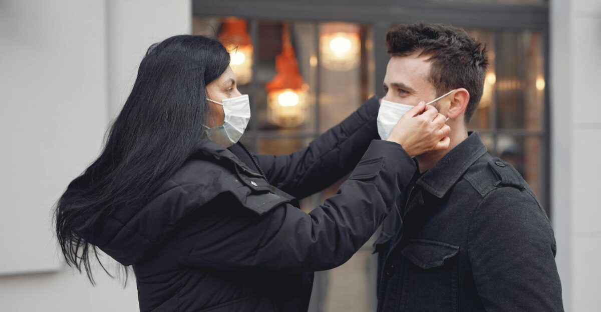 A woman adjusts a man s face mask on a city street promoting health and safety