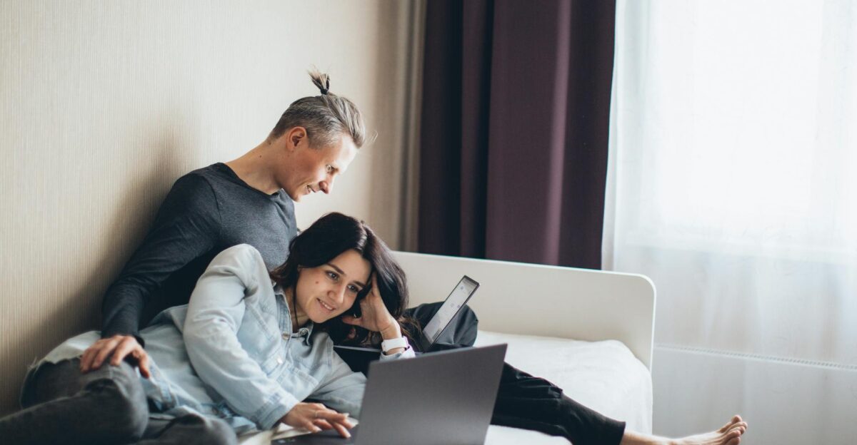 Happy couple working remotely on laptops in a cozy bedroom setting