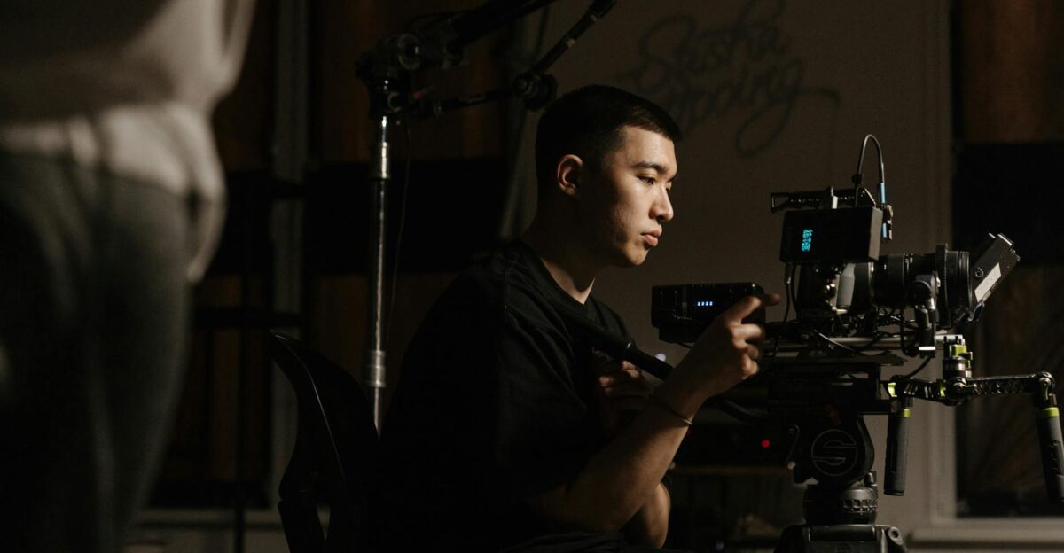 Side view of cameraman operating professional equipment during film production indoors