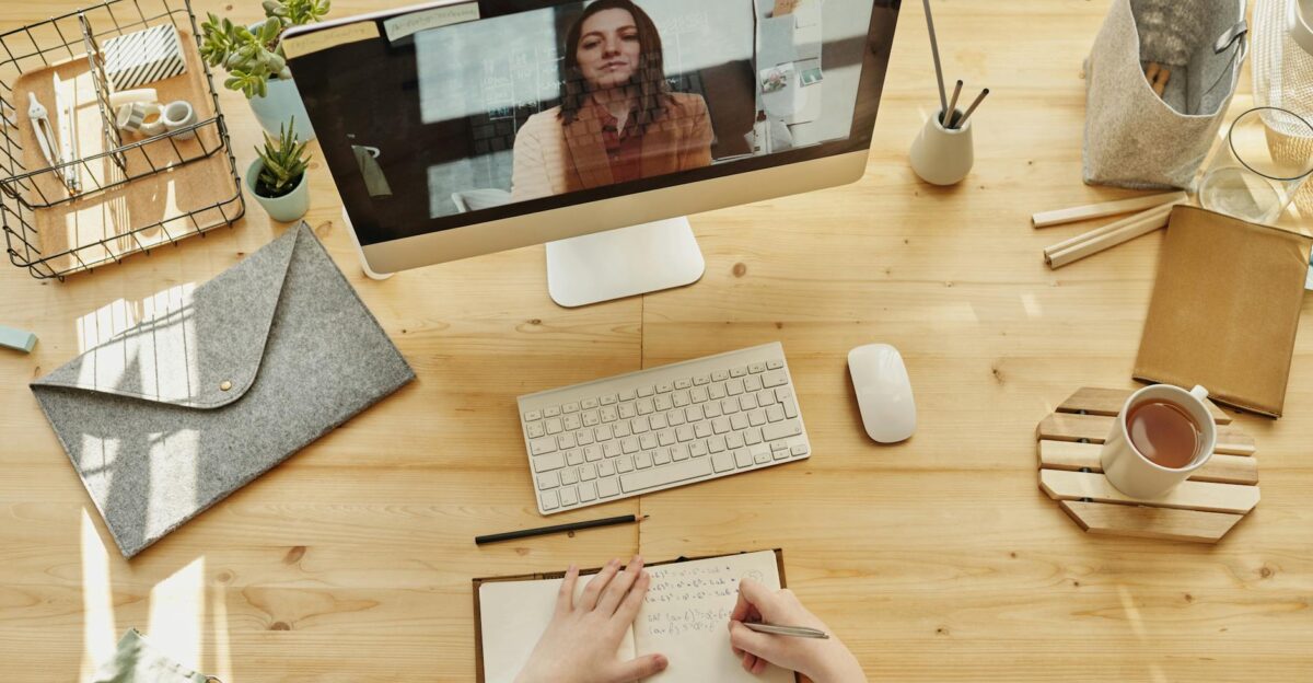 Person taking notes during a video call at a neatly organized home desk showing remote work lifestyle