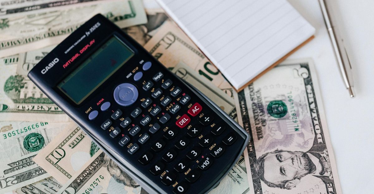 From above electronic calculator and notepad placed over United States dollar bills together with metallic pen for budget planning and calculation
