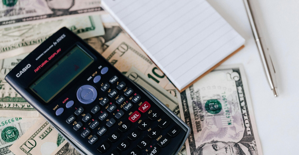 From above electronic calculator and notepad placed over United States dollar bills together with metallic pen for budget planning and calculation